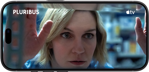  iPhone 18 Pro, modo horizontal, primer plano de una mujer que mira a través de una ventana. Título de la serie: Pluribus